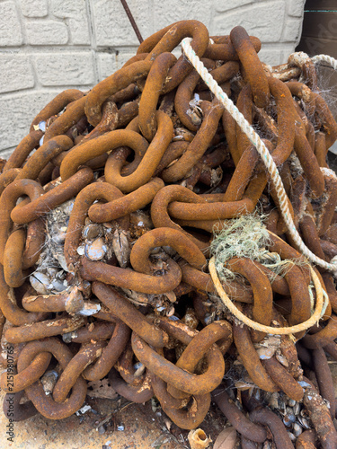 Foto A large pile of heavily rusted anchor chain encrusted with mussels and sea debris, lying on a concrete surface near a stone wall at a harbor