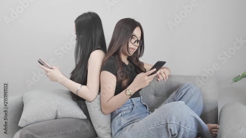 Two Asian Women Sitting Back to Back and Looking at Their Smartphones