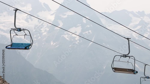 Empty chairlift seats moving against misty snow mountain peaks