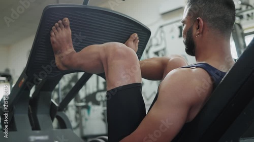 A young Indian Asian fit, muscular, confident male or man performs a leg press exercise during a resistance weight training workout in a modern gym. Fitness, health, bodybuilding, wellness concept.