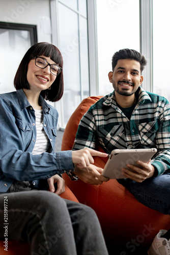 A woman with glasses and a man in a plaid shirt smile while looking at a tablet, suggesting teamwork and modern communication