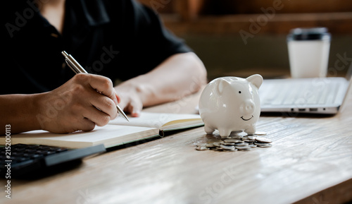 Person putting a coin into a piggy bank while using a calculator, symbolizing saving money, budgeting, financial planning, and personal finance management.