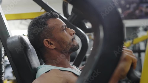 An Indian Asian fit healthy elderly or old man performs resistance or weight training exercise using a machine in a modern gym. Fitness, workout, healthy lifestyle, wellness. bodybuilding concept