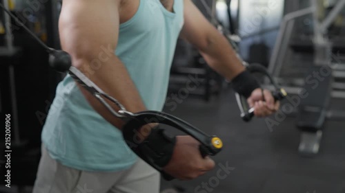 Side view of a young Indian Asian fit, muscular man performing a standing cable chest fly exercise during a resistance training session in a modern gym. Wellness, fitness, weight training concept