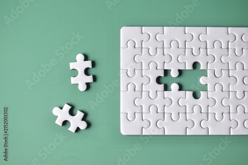 Фотография Top-down view of an unfinished white jigsaw puzzle on a mint green background with a large gap and two separate matching pieces laying to the left