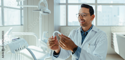 Male dentist examining clear aligner in modern dental clinic portrait