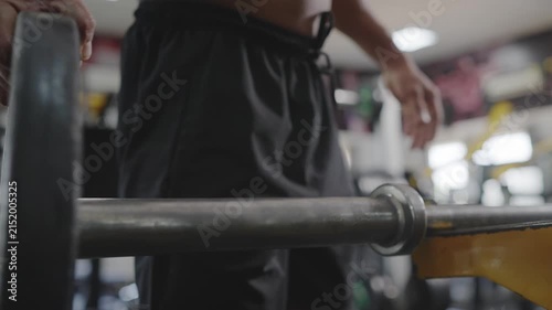 A close up view of an Indian Asian fit, muscular man or male adding weight plates to a barbell before performing a resistance weight training exercise in a modern gym. Fitness, bodybuilding concept