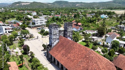 Cinematic drone footage gradually pulling backward and ascending away from Mang Lang Church, a historic Catholic church in Vietnam. 