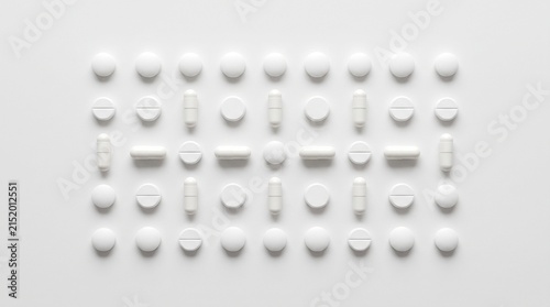 A collection of various white pills arranged in rows and columns against a light background.