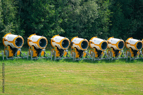 Fotografie a row of modern white and yellow snow cannons is lined up neatly on a green gras