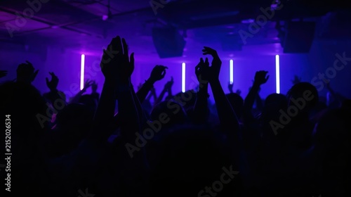 Crowd of people with hands raised dancing in nightclub under purple neon light. Silhouette of woman and man enjoying electronic music at dance festival. Nightlife party entertainment.