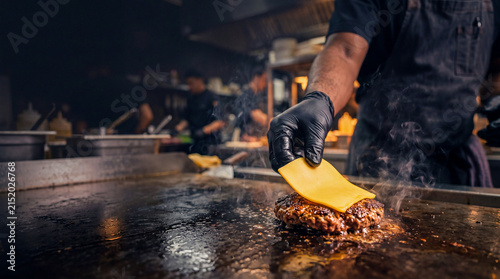 Chef Cooking Burger: A chef in a professional kitchen expertly cooks a juicy burger on a hot griddle, melting a slice of cheese on top, capturing the essence of culinary craftsmanship.