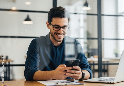Smiling young businessman using smartphone while working in modern office