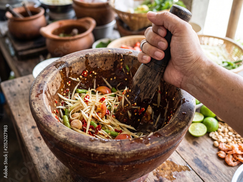 Hand pounding spicy Thai green papaya salad som tum in rustic wooden mortar
