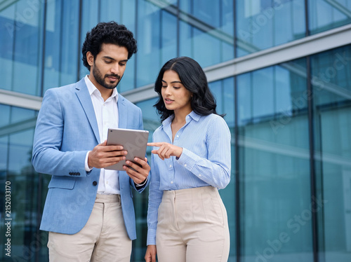 young Indian business professionals reviewing information on a tablet with a businessman holding the device while a businesswoman explains during a corporate consultation