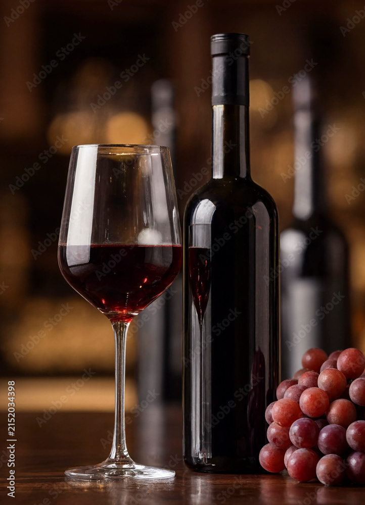 Fototapeta premium A bottle of red wine with a filled glass and a cluster of grapes on a warm blurred background. The composition evokes tasting, dining, and cozy evening ambiance.