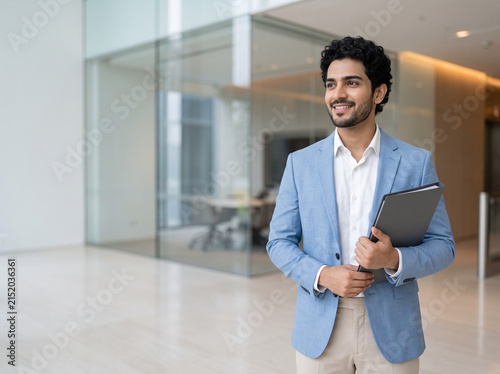 young Indian male business professional holding a document file in a luxury corporate office with clean copy space for finance consulting and business advertising