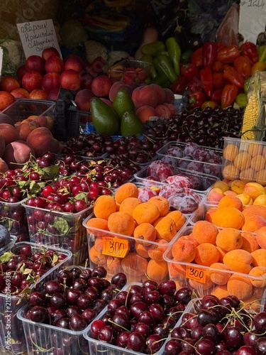 Fresh seasonal fruits, berries, vegetables and herbs displayed at a local farmers market stall. Colorful assortment of natural produce including apricots, plums, cherries and greens.