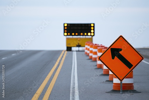 Orange traffic cones and arrow sign mark lane closure, with warning lights ahead