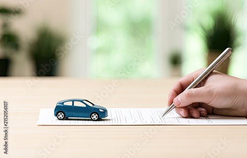 Hand signing document next to a miniature blue car