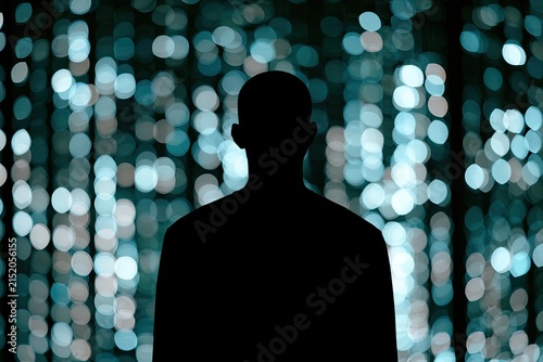 Silhouette of a person against a backdrop of shimmering, out-of-focus blue and white lights