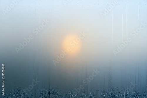 Soft sun obscured by foggy window pane with water droplets