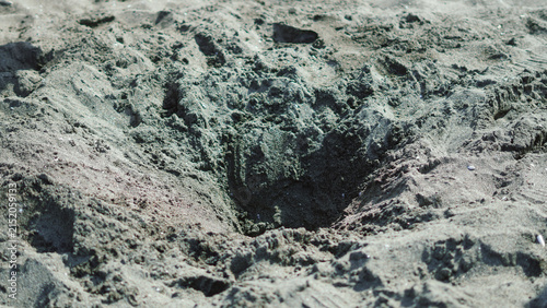 A deep hole dug in the dark sandy beach ground.