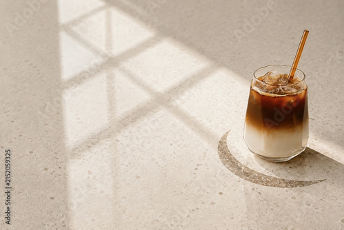 Layered iced coffee with milk and glass straw in warm sunlight