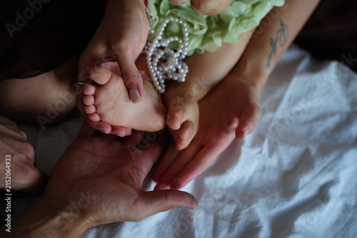 Hands gently cradle a baby's tiny feet, symbolizing care and tenderness. The image captures a moment of warmth and connection between family members in a serene setting.