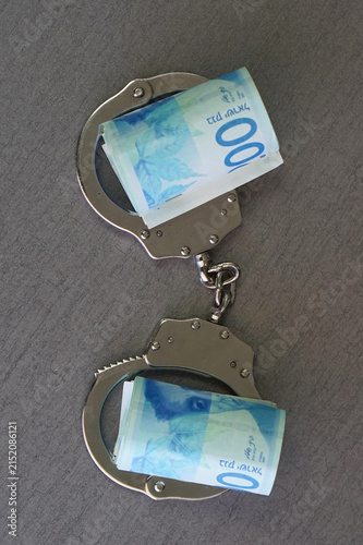 Handcuffs hold rolled 200 Israel shekel banknotes. Currency suggests financial constraint or legal issues