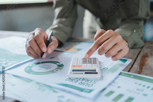 ESG investment sustainable finance concept, professional hands using calculator and pen for environmental performance metrics and carbon footprint corporate responsibility report analysis.
