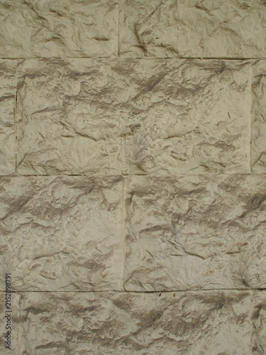 A vertical close-up picture highlighting the coarse surface and natural relief of light beige stone cladding blocks. Detailed and tactile background of building material