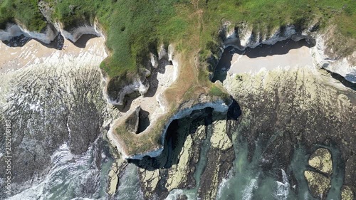 Aerial top down tracking view over rugged chalk cliffs and sea caves at Flamborough, England