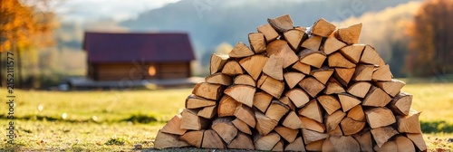 A Large Stack of Chopped Firewood Resting Beside a Cozy Countryside Cabin in an Autumn Landscape