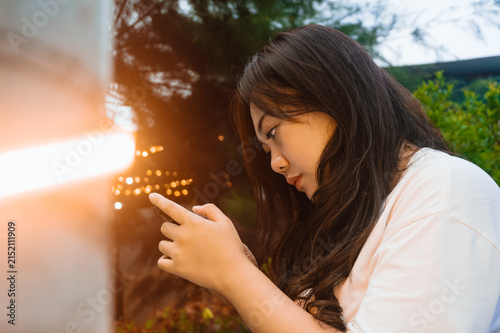 Fotografie Young woman engrossed in mobile phone with cinematic lens flare, concept of digital addiction, social media usage, or screen time