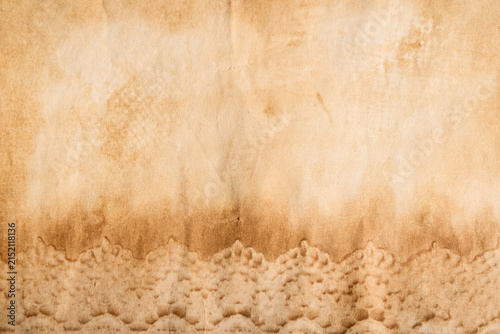 Old vintage paper texture. Light brown aged paper with faded stains, subtle creases and delicate lace imprints along the bottom edge.