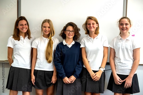 Five students in uniforms standing in front of a whiteboard  smiling.