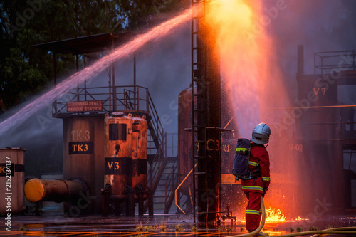 Firefighter wearing protective gear using a hose to extinguish a fire outside a building