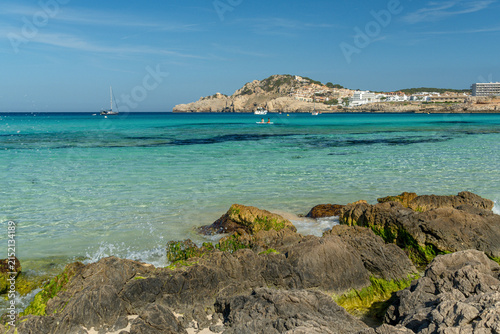 Crystal Clear Turquoise Water at Cala Agulla Beach with Rocks and Hillside Coastline in Mallorca