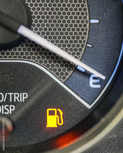 Macro close-up of a car dashboard fuel gauge needle pointing to empty (E), with a fuel pump warning icon illuminated, Low Fuel Warning Light on car Dashboard Display