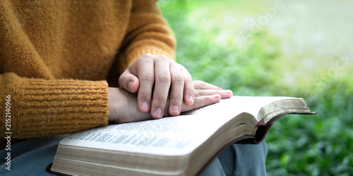 Fotografie A young girl sits praying to God, her hands clasped open, amidst an open natural setting, symbolizing faith, hope, spiritual guidance, and the Holy Word