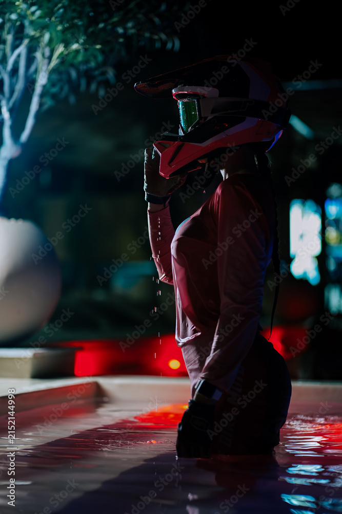 Obraz premium Motocross rider standing in a swimming pool at night while wearing a protective helmet and gear