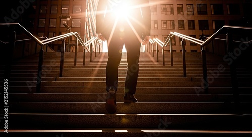 Businessmen climbing concrete stairs towards bright sunlight symbolizing career growth and ambition