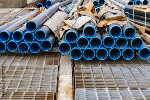 Industrial metal pipes with bright blue inner plastic lining stacked on steel drainage grates at construction site or port