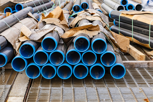 Industrial metal pipes with bright blue inner plastic lining stacked on steel drainage grates at construction site or port