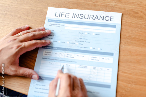 Canvastavla Person filling out a life insurance form on a wooden table.