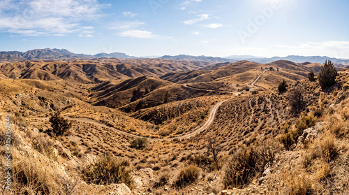 View of rolling hills and valleys in a dry landscape with winding road under clear sky Generative AI