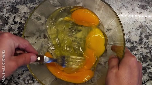 Manos batiendo huevos crudos con un tenedor en bowl de vidrio