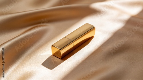 Luxury gold lipstick case lying on soft satin silk fabric in warm sunlight ideal for high end cosmetic brand advertising and makeup marketing
