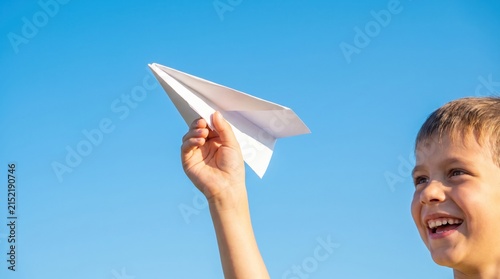 Happy Boy Playing with Paper Airplane Against Clear Blue Sky Outdoors